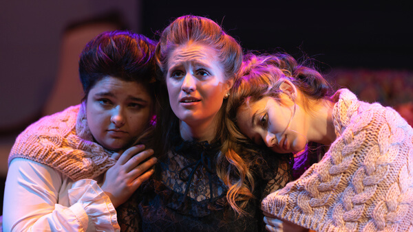 Two women hang on either side of the third looking serious during the "Three Sisters" production
